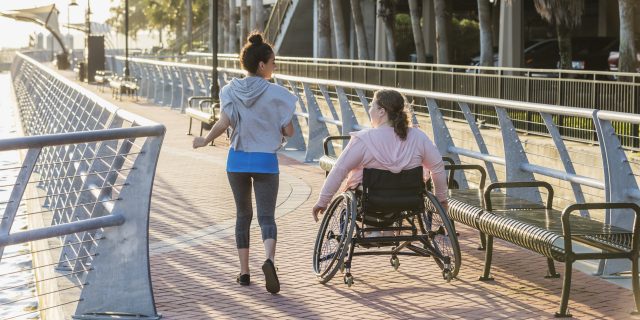 ng woman with spina bifida, and a friend on a city boardwalk.