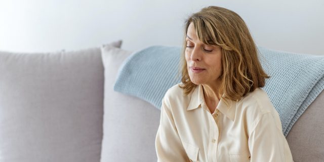 Woman sitting on gray sofa, looking down with her arms wrapped around herself