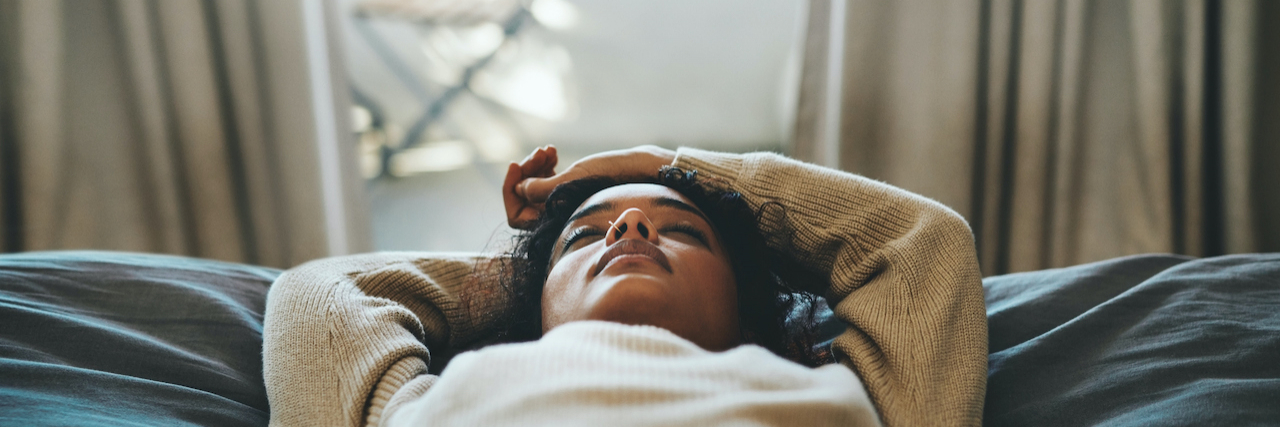 Cropped shot of a woman of color lying on her bed with her eyes closed