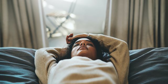Cropped shot of a woman of color lying on her bed with her eyes closed