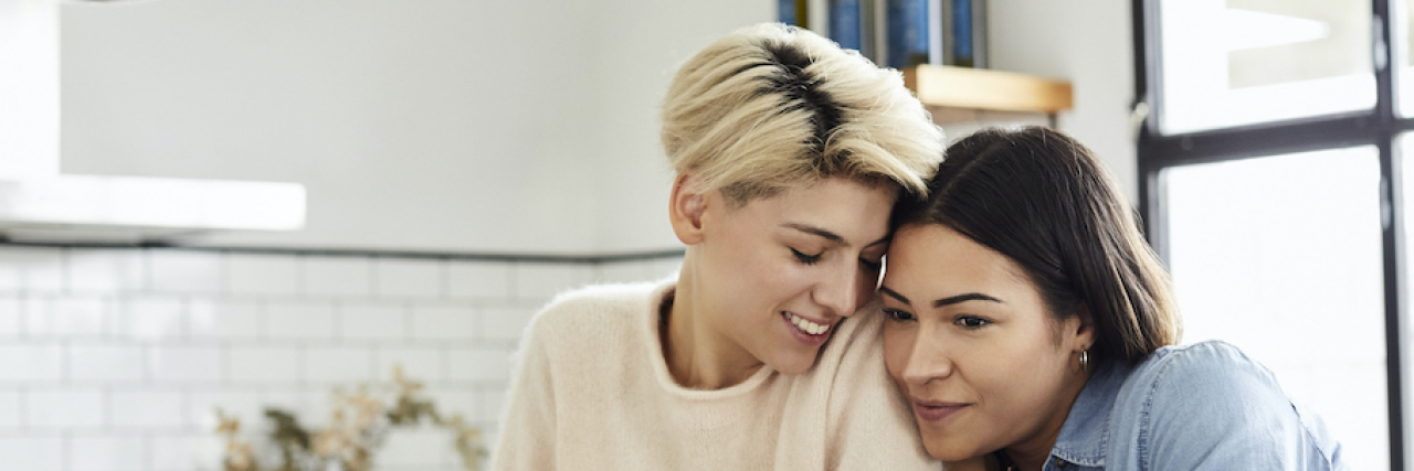 Two women snuggling as a couple at home in the kitchen