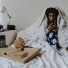 Young woman using smart phone while sitting in bedroom