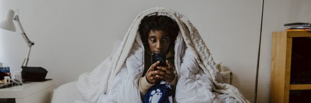 Young woman using smart phone while sitting in bedroom