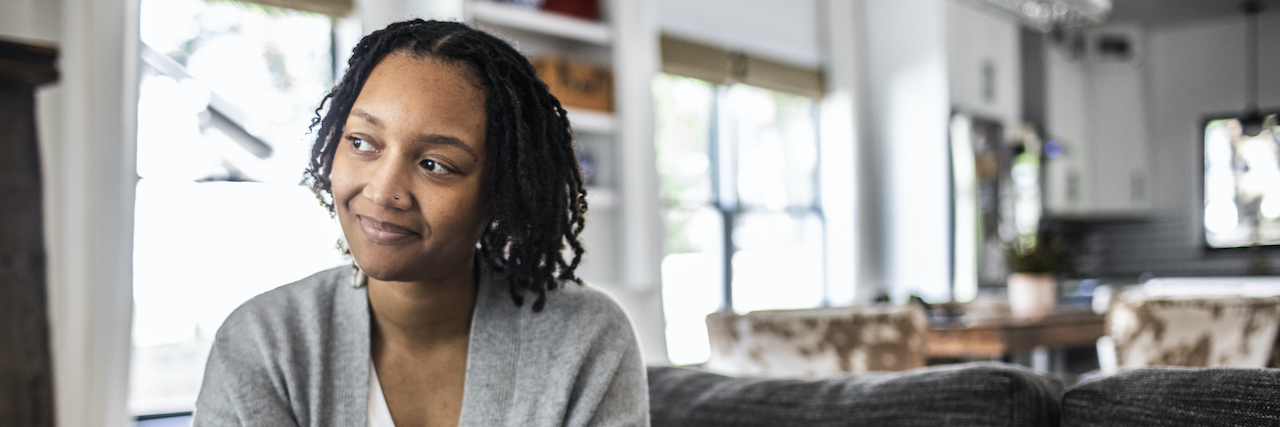 Thriving in Spite of Childhood Abuse and Trauma Black woman holding phone on sofa at home, smiling slightly and looking to the side