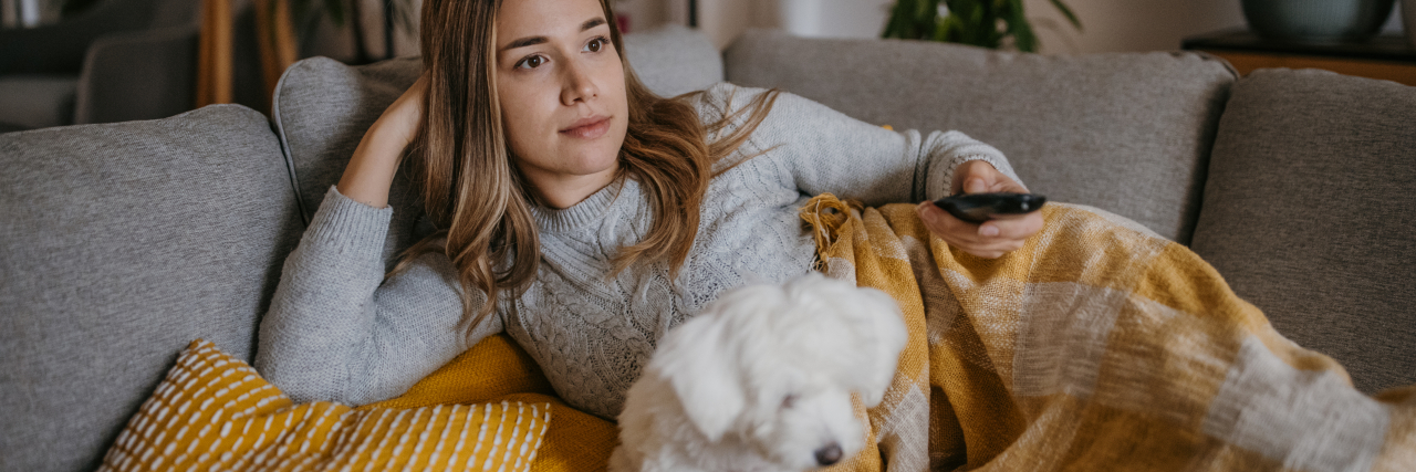 Woman watching television with her Maltese puppy on sofa at home.