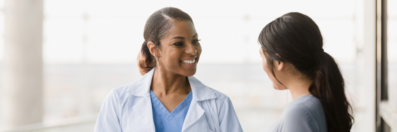 18 Things People With Chronic Illness Wish Their Doctors Would Say A Black doctor smiles and talks with her patient, holding a clipboard