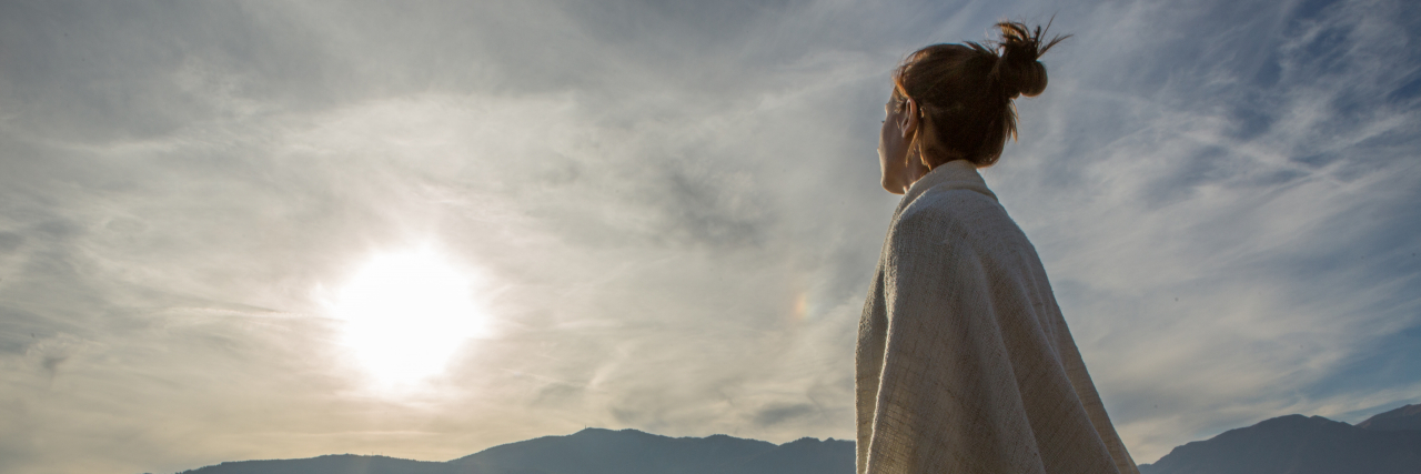 Why a Good Day With Chronic Illness May Be Bad for Our Mental Health Woman watching sunset over lake.