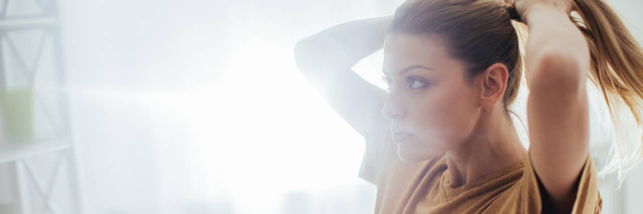 Beauty and Style Life Hacks for Hard Mornings With Depression Woman looking in a mirror, putting her hair in a ponytail