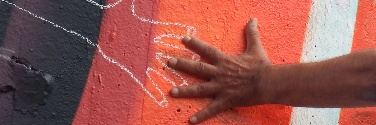 A hand reaching out to another chalk drawn illustration of a hand against street art
