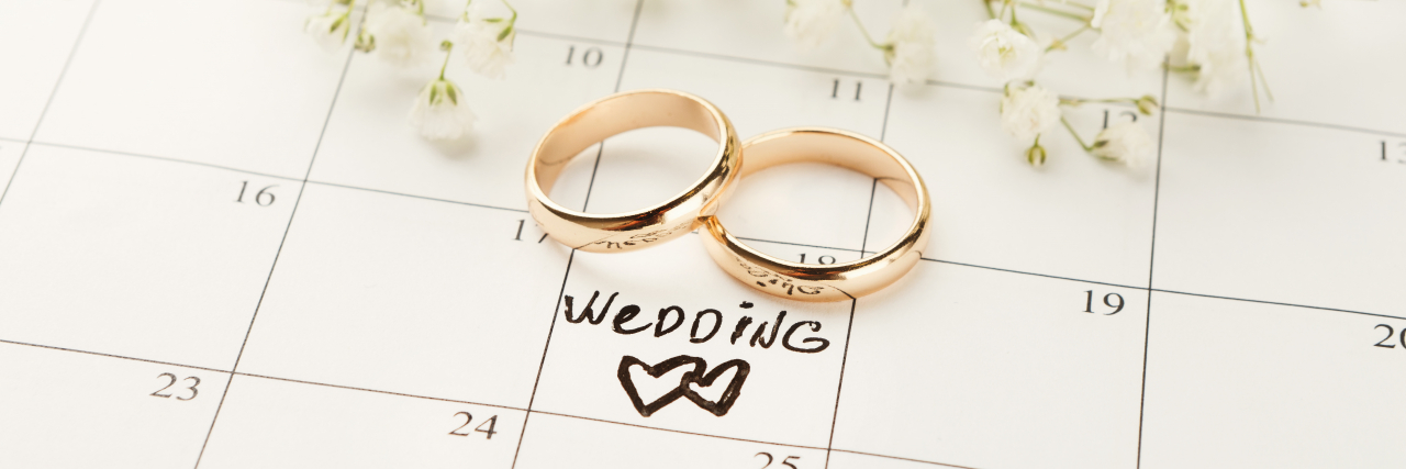 7 Tips for Planning a Wedding During an Endometriosis Flare Word wedding, two hearts and gold rings on calendar with sweet white flowers.