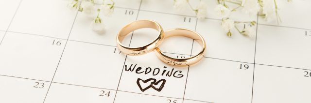 Word wedding, two hearts and gold rings on calendar with sweet white flowers.