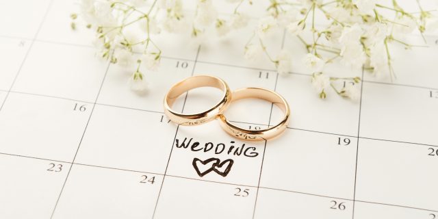 Word wedding, two hearts and gold rings on calendar with sweet white flowers.