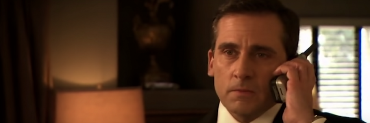 Michael Scott from "The Office" taking a phone call in a suit in a dimly lit room.