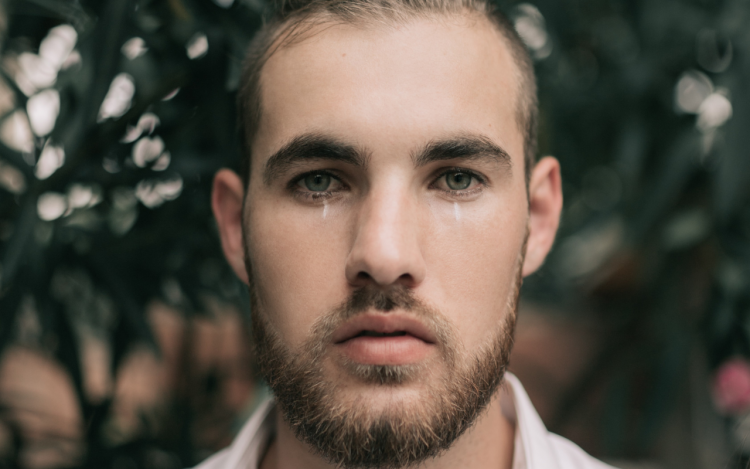 man standing in front of flowers looking into camera and crying