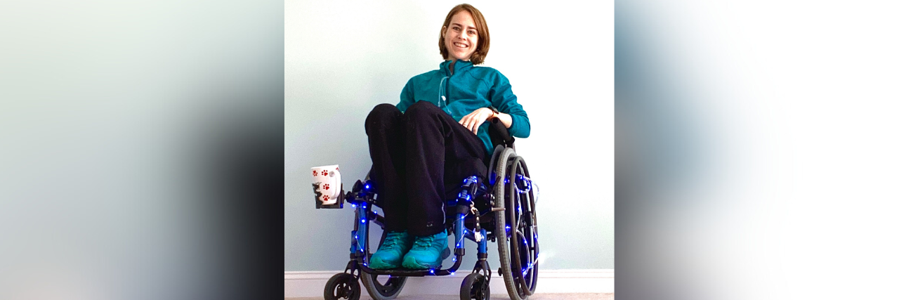 Woman sitting in wheelchair and smiling, with cup holder attached to it