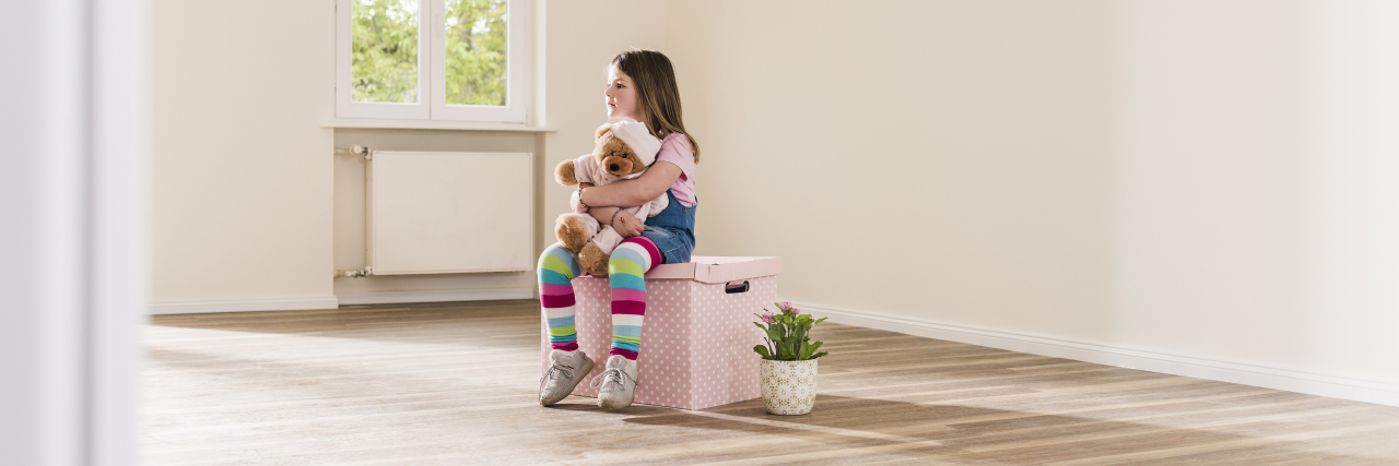 A young girl sits on a pink box in an empty apartment.