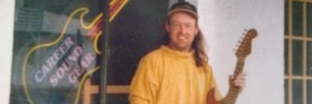 Suddenly Losing a Stepbrother to Chronic Illness as an Adult The author's friend, a man with long, red hair holds a guitar while standing next to a guitar display.