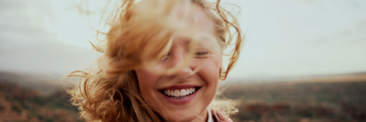 How Saying No to Sex Without Explanation Is an Act of Self-Care Woman standing outside above a valley, smiling as the wind whips her auburn hair around her face