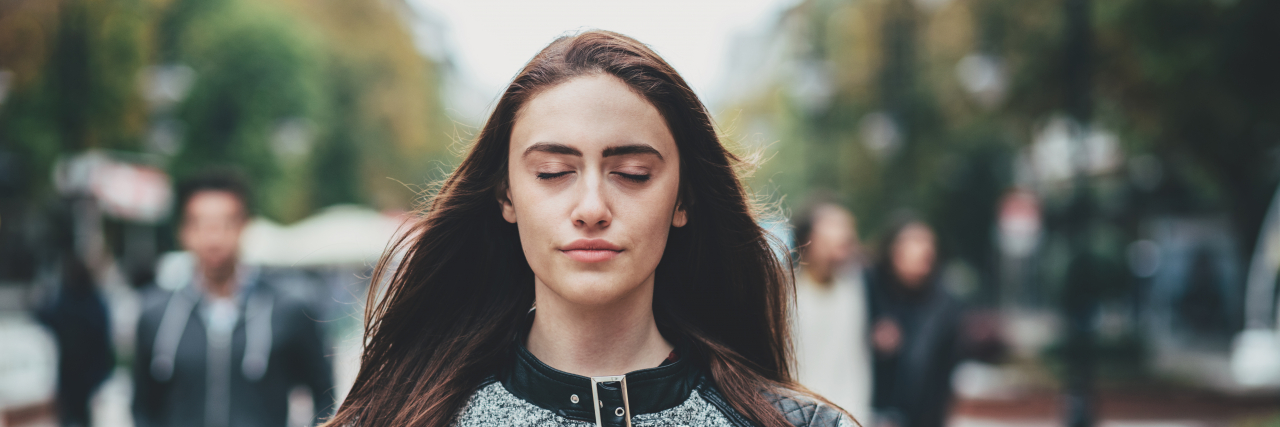Lessons Learned From Grieving an Unexpected Diagnosis A woman with long brown hair wearing a gray coat stands and breathes with her eyes closed.