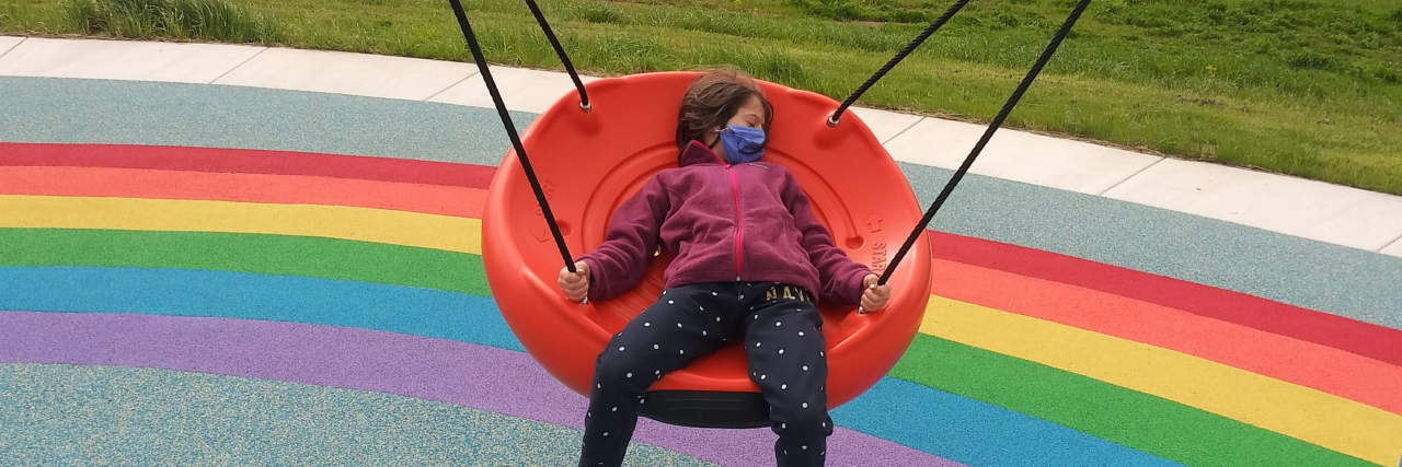 Happy child on swing with rainbow painted on pavement.