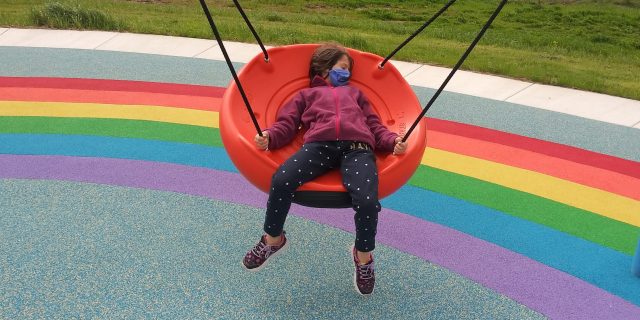 How Non-Disabled Allies Can Help Make Society Inclusive Happy child on swing with rainbow painted on pavement.