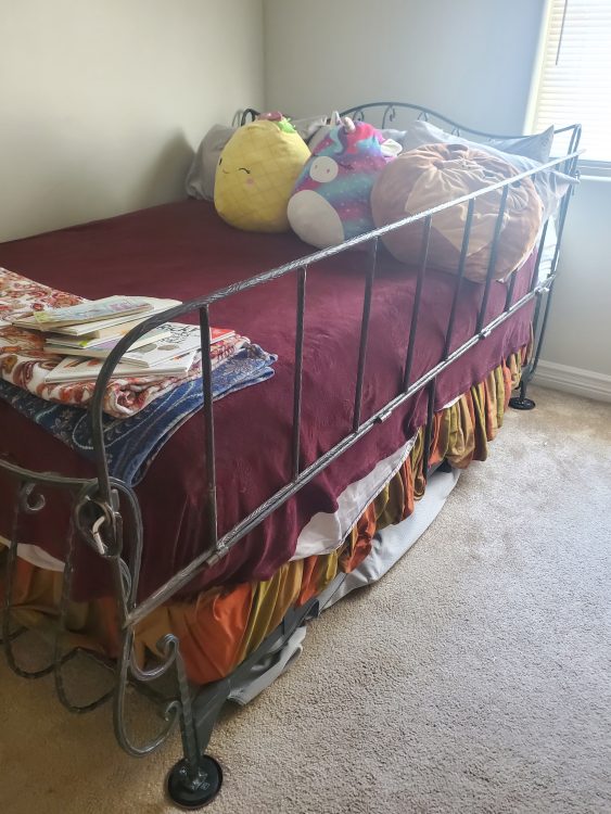 A bed with red sheets, guardrails, and several stuffed animals.