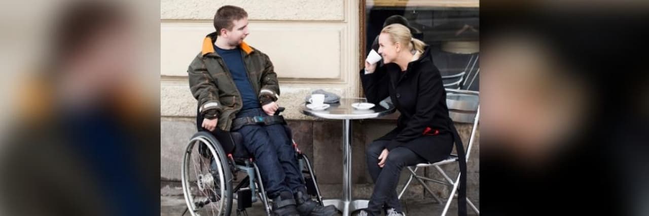 Female caregiver and disabled man having coffee at sidewalk cafe