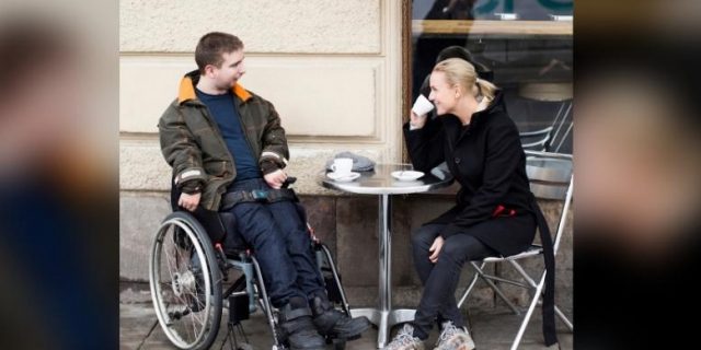 Female caregiver and disabled man having coffee at sidewalk cafe