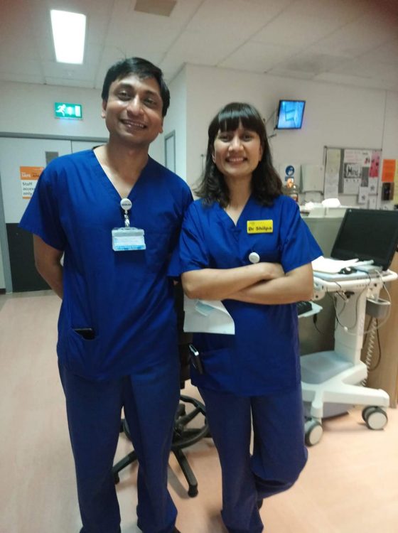 The author, a man with black hair and eyes wearing blue scrubs stands in the hospital alongside a woman in blue scrubs.