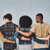 Rearview studio shot of a diverse group of young people embracing each other against a gray background