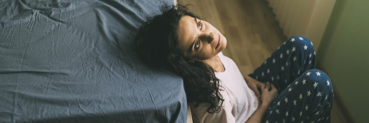 A woman sitting next to her bed looking up.