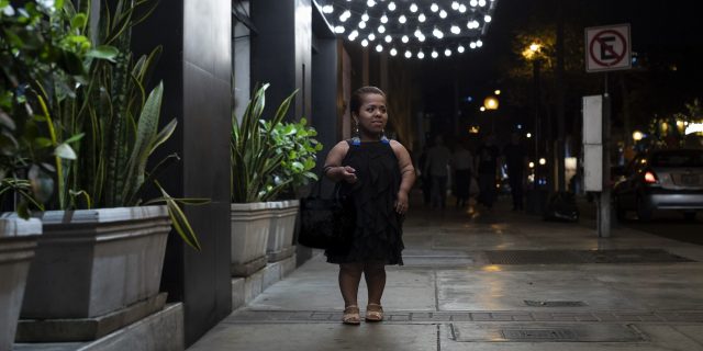 Woman with dwarfism walking outside a club at night.