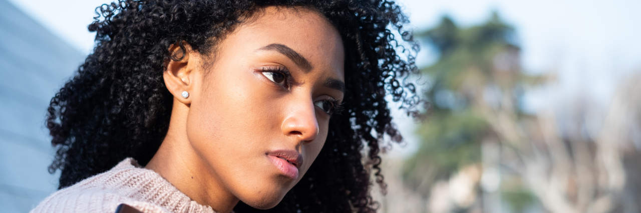 Coping With Rejection-Sensitive Dysphoria in High Rejection Rate Jobs Black woman using mobile phone staring forlornly into the distance in a sweater outside.