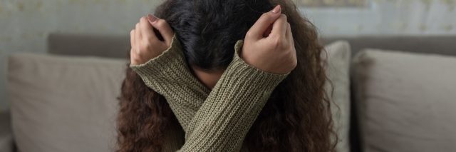 photo of woman covering her face in her arms in an X shape, looking upset