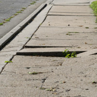Uneven damaged sidewalk, tripping hazard.
