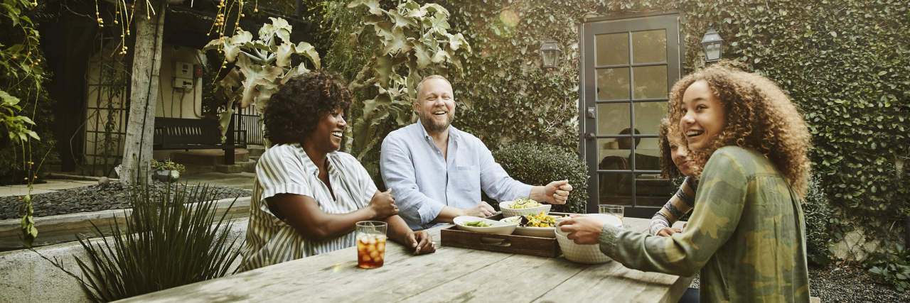 Why Relationships Matter With NMOSD Laughing family sharing meal at picnic table in backyard