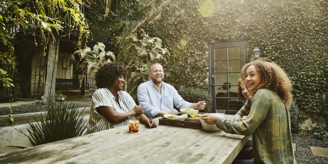Laughing family sharing meal at picnic table in backyard