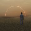 surreal photo of a man walking in a field at sunset with an arc of light in the background