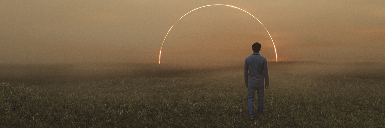 Dreamy surreal photo of a man walking in a field at sunset with an arc of light in the distance ahead.