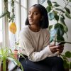 Black woman at home surrounded by plants and looking out window
