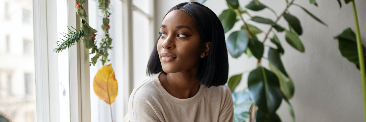 The Subtle Warning Signs of a Depressive Episode Black woman at home surrounded by plants and looking out window