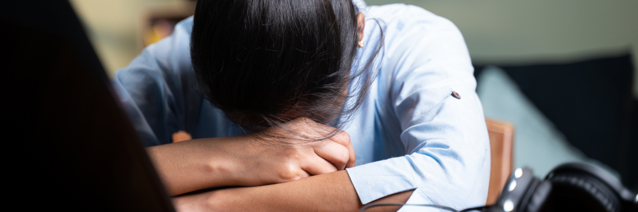 How to Take a Mental Health Break From Work photo of a young person resting their head on their arms in front of a laptop, looking upset