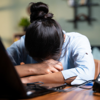 photo of a young person resting their head on their arms in front of a laptop, looking upset