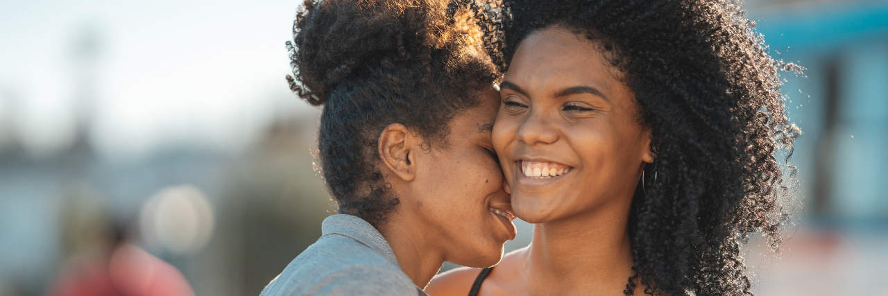 Are You Crushing or Hyperfixating on That Person? Two young women where one is kissing the other's neck. It's daylight out and one is in a cut off shirt and the other is in a Black top. They're very happy and in love!