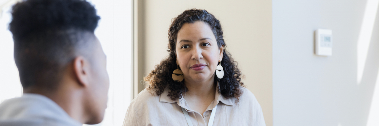 Important Questions to Ask Your New Therapist at Intake Counselor, a woman of color, listens and holds a notebook during a session with a young man