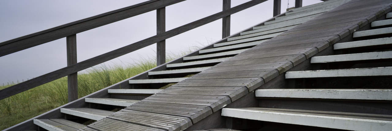 Include Disabled People When Designing Accessible Architecture Section of a wooden stairway with steep ramp leading over the dunes towards the beach.