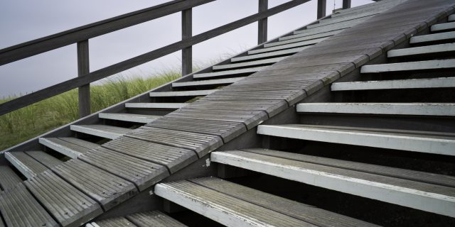 Section of a wooden stairway with steep ramp leading over the dunes towards the beach.