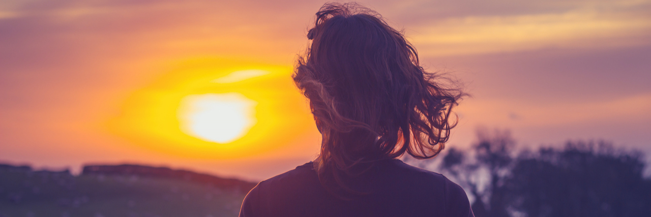 How Having a Disorganized Attachment Style Makes Me Unpredictable Woman admiring the sunset over a field from her balcony, seen from behind