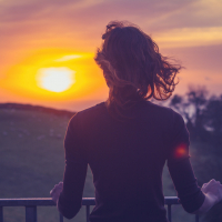 Woman admiring the sunset over a field from her balcony, seen from behind