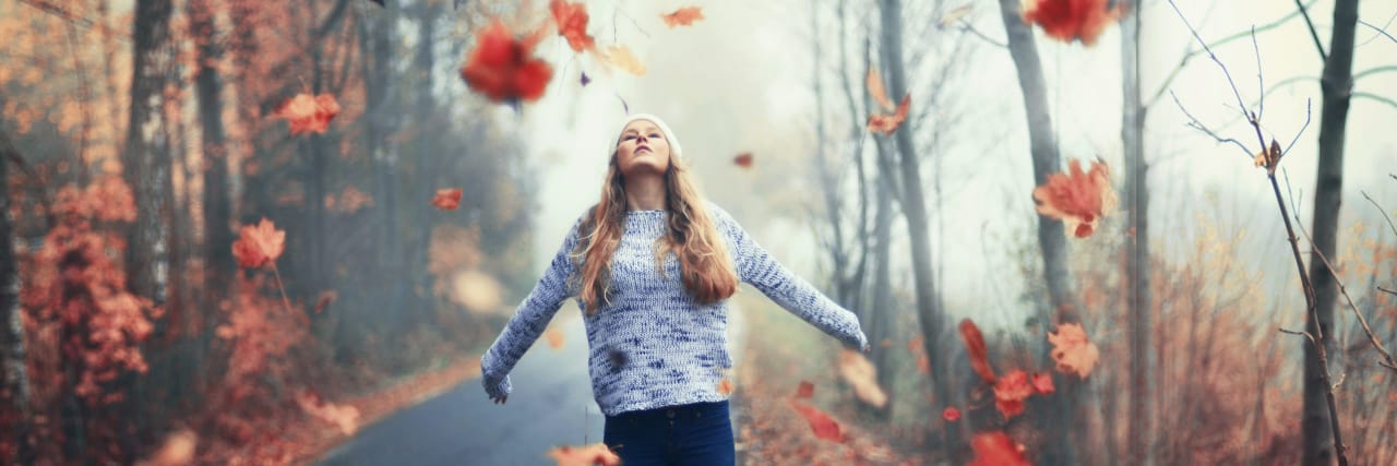Letting Go of the 'Could Haves' and 'Should Haves' When You're Disabled Woman with arms outstretched and leaves blowing in the wind.